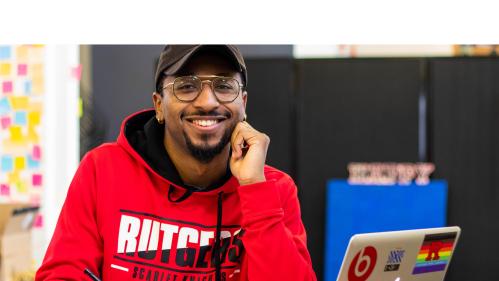smiling student wearing Rutgers sweatshirt studying on his laptop