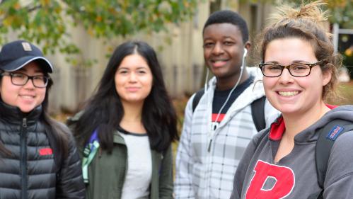 group of four smiling students standing together outside