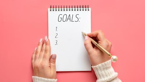 female hand holds pen and writes a list of goals