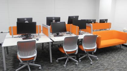 A computer lab with white desk, white chairs with orange padding and an orange couch.
