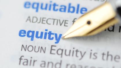A gold tipped pen is pointing to the word equity in the dictionary