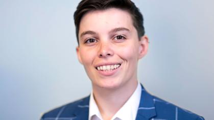 Brittany is smiling and has short cropped hair and is wearing a blue and white checkered suit with a white collared shirt
