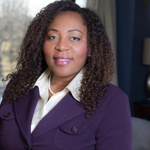 Francine Conway is an african american woman with long curly hair. She is wearing a purple jacket, a white collared shirt and a pearl necklace