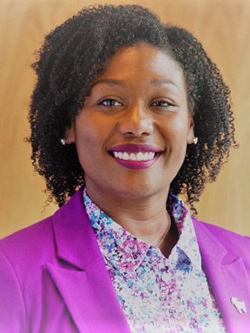Tiffiny Butler - an African American woman with curly hair smiling. She is wearing a floral collared shirt under a pink jacket