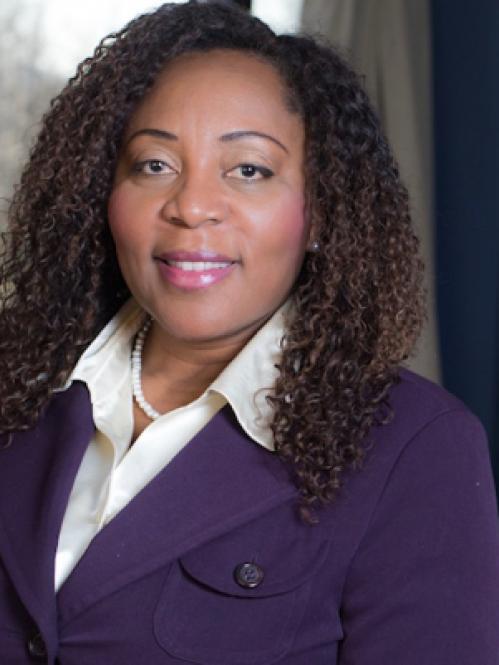 Francine Conway is an african american woman with long curly hair. She is wearing a purple jacket, a white collared shirt and a pearl necklace