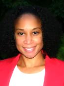 Kimberley is an african american woman with curly shoulder length hair. She is wearing a red blazer with a white blouse underneath.
