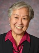 Lily is an asian american woman with short grey hair. She is smiling and wearing a red collared shirt under a black blazer.