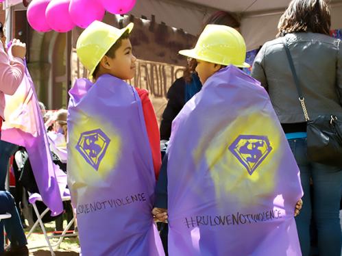 2 young boys standing together wearing purple capes with the superman "S" and the #lovenotviolence written on them with a black marker