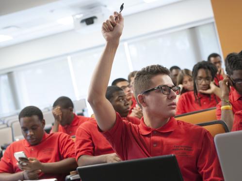 Male Student raising his hand in the classroom of a diverse group of students all wearing red shirts