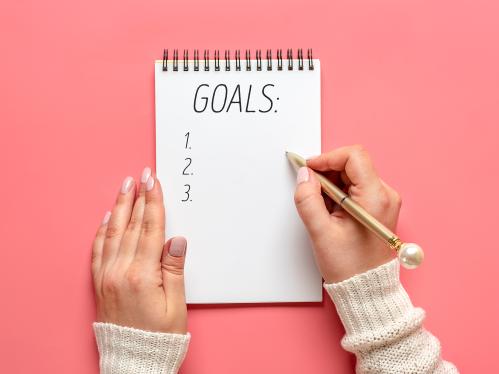 female hand holds pen and writes a list of goals