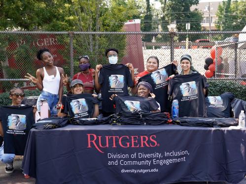 A diverse group of students from the Paul Robeson Success Institute BBQ closing event holding up t-shirts with Paul Robeson's face 