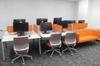 A computer lab with white desk, white chairs with orange padding and an orange couch.